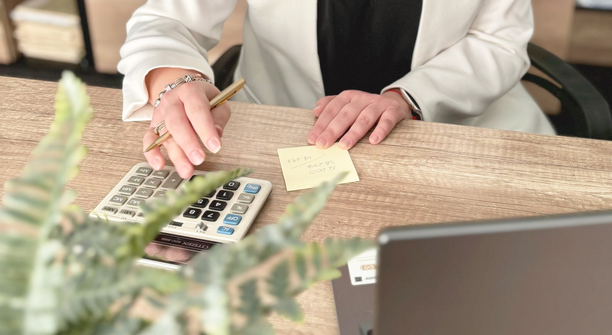Zbliżenie na dłonie księgowej z kalkulatorem i notatką.